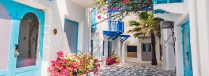 Whitewashed houses with blue doors and blooming flowers along a narrow street in Mykonos, Greece