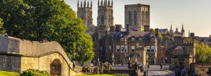 View of York Minster rising above the historic York City Walls and traditional buildings in York, England, on a sunny day.