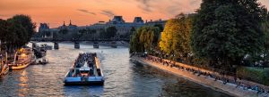 Evening boat cruise along the Seine River in Paris, France with historic bridges and glowing city lights at sunset.