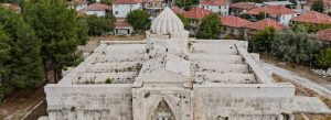 Historic Ottoman caravanserai building in Turkey surrounded by traditional village houses and trees.