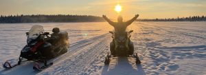 Guided snowmobile excursion across a frozen landscape in Kiruna, Swedish Lapland during a golden Arctic sunset.
