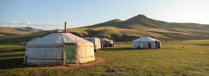 Traditional Mongolian gers in a nomadic encampment surrounded by green grasslands and rolling hills