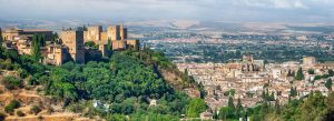 Panoramic view of the Alhambra palace and fortress overlooking Granada, Spain, surrounded by green hills and historic city buildings.